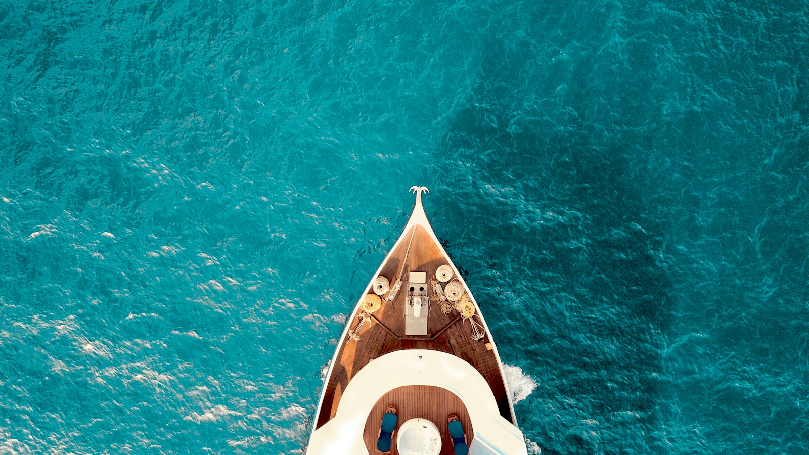 Bow of a yacht on turquoise water seen from above